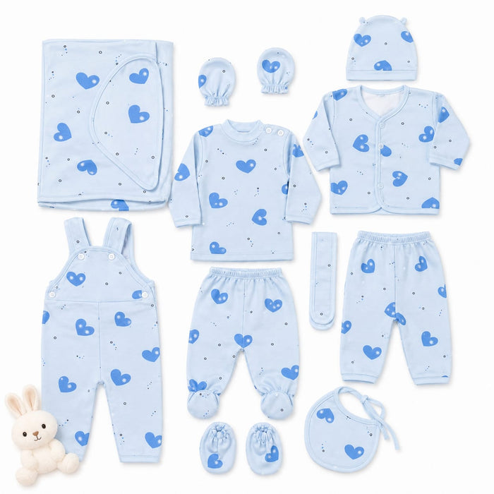 A baby clothing set laid out on a white background, including a light blue long-sleeve top, matching footed pants, overalls, a cardigan, a bonnet, a bib, a hat, a muslin cloth, and booties, all printed with a blue heart pattern. A small plush bunny toy is