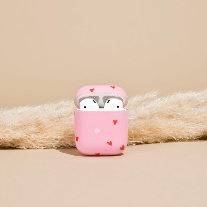 Pink Coconut Lane AirPods case with red hearts, holding white earbuds, on a beige fluffy surface.