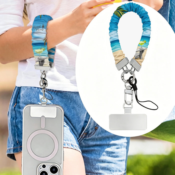 Blue and green satin Beach Please scrunchie phone wrist strap clipped to the matching Beach Please Wavy Luxe iPhone case with a beach chair and cocktail design, styled on a sandy shoreline background with starfish and ocean waves.