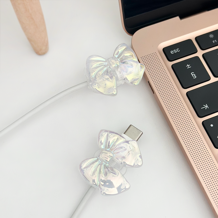 Lilac holographic bow USB-C cable from Coconut Lane plugged into a rose gold laptop on a white surface.