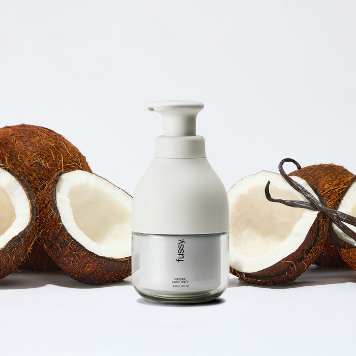 Fussy's natural, refillable Coconut Milk body wash in a white pump bottle, set against a background of coconuts and vanilla pods