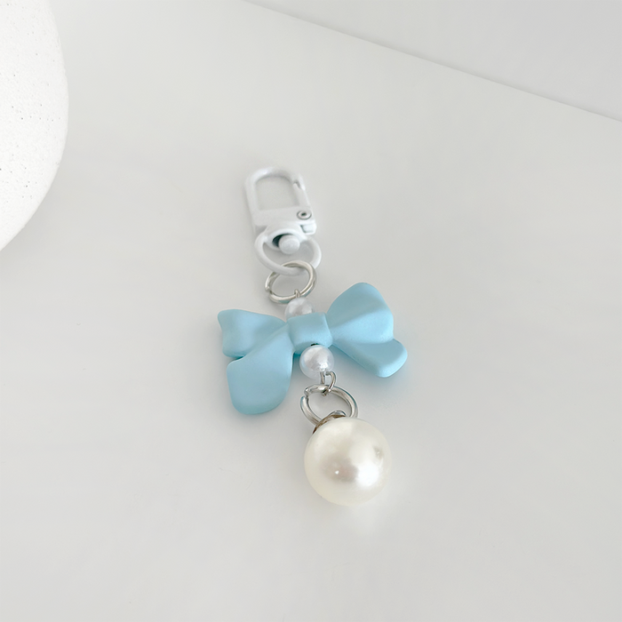 Light blue bow keyring with a white pearl charm, displayed on a white background.