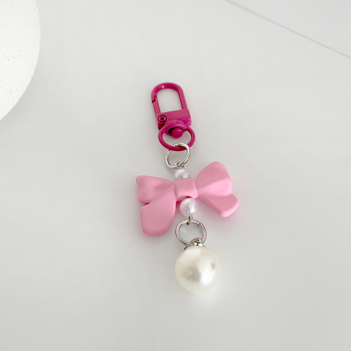 Bright pink bow keyring with pearl charm and pink clasp on a white surface.