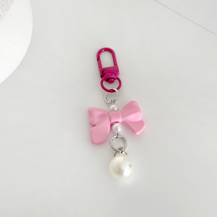 Bright pink bow keyring with faux pearl charm and pink clasp on a white surface.