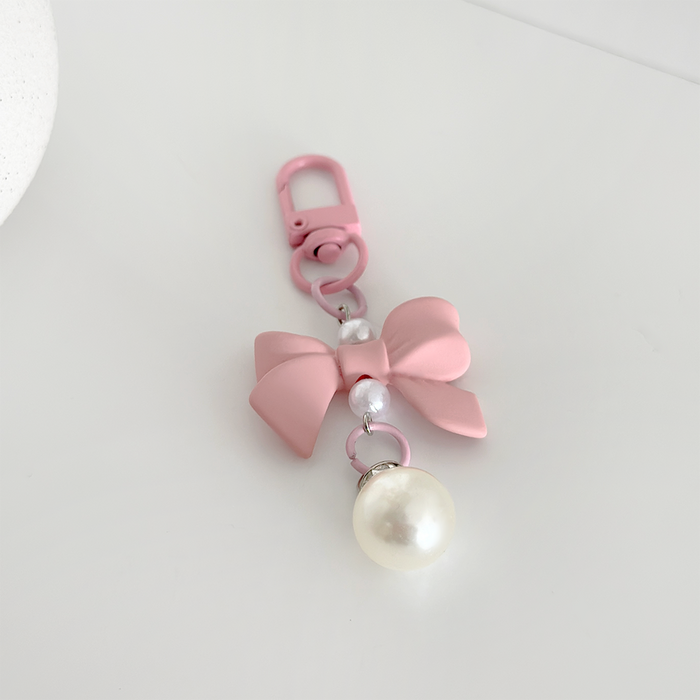 Peach pink keyring with a bow, heart charm, beads, and faux pearl on a white base.