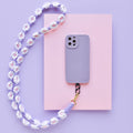 Lilac crochet flower phone lanyard bundle on pink paper with a purple background.