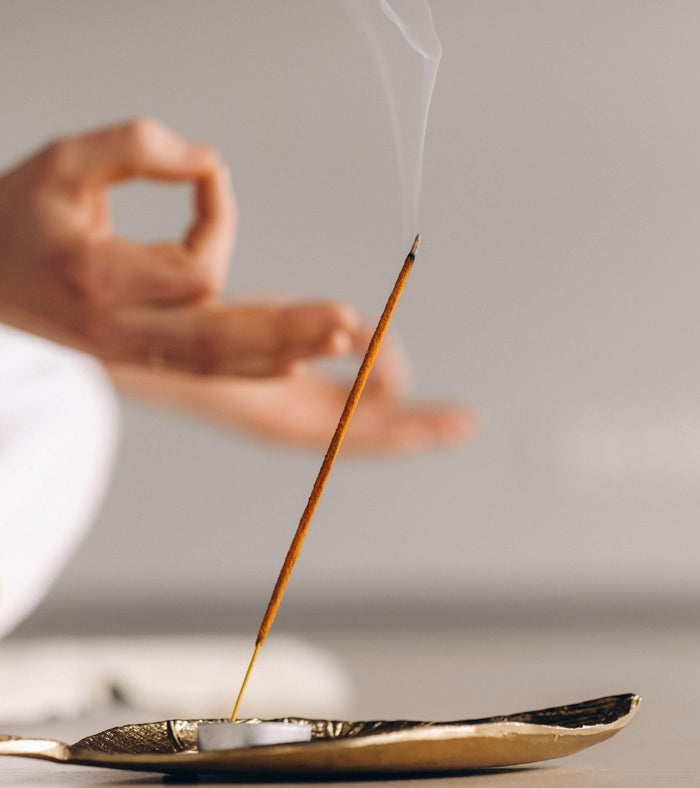 Hand lighting an incense stick with smoke rising from a small metal incense holder