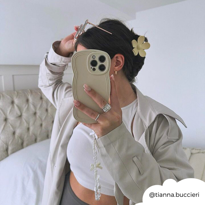 Woman in neutral outfit takes mirror selfie, hair up with cream Coconut Lane flower claw clip, holding beige phone.