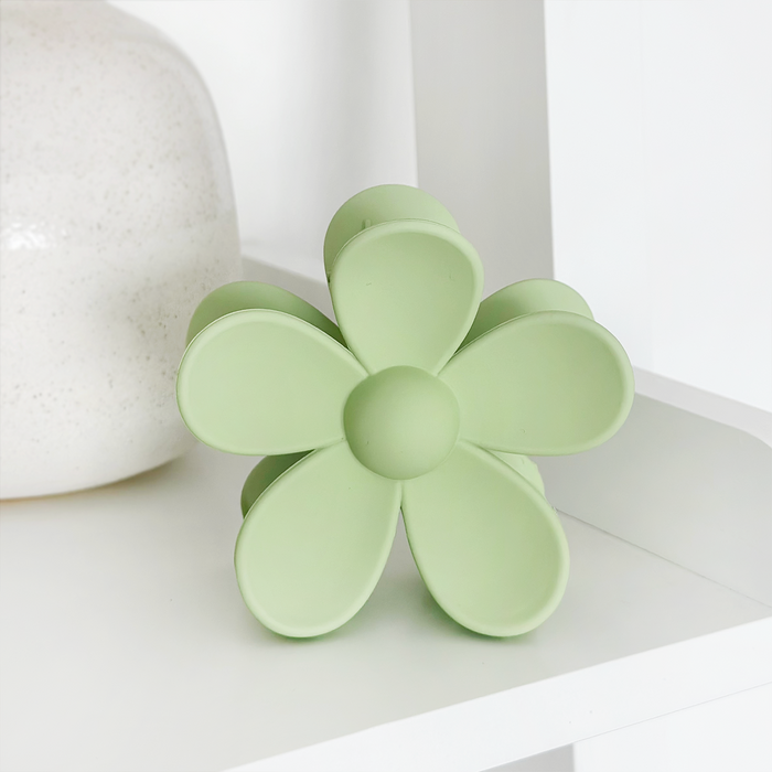 Green Coconut Lane flower claw clip with five petals displayed on a white shelf beside a speckled white vase.