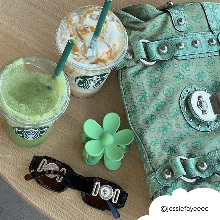 Starbucks drinks, sunglasses, a mint-green purse, and a green flower claw hair clip on a wooden table.