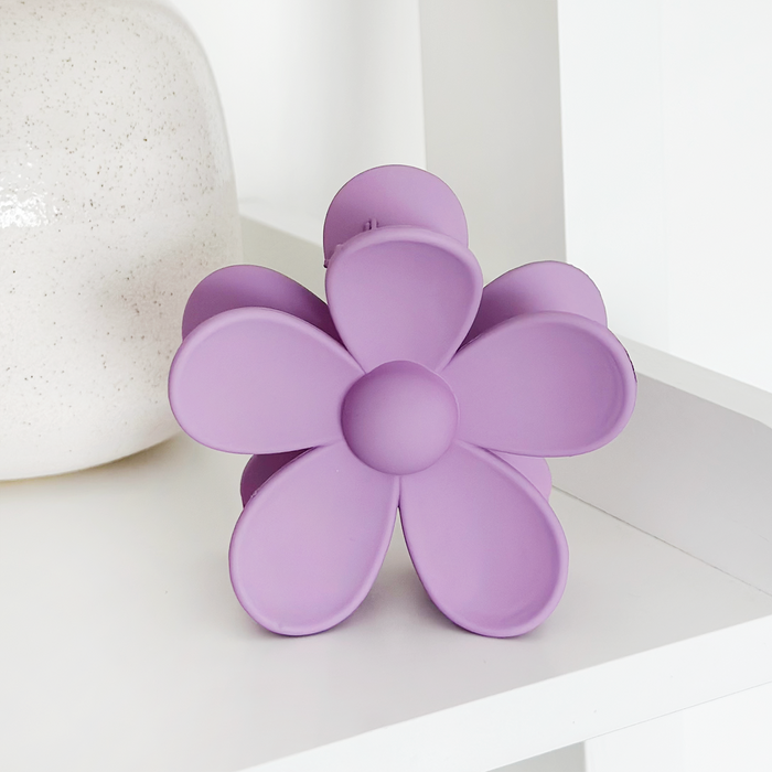 Lilac flower-shaped claw clip displayed on a white shelf beside a white vase.