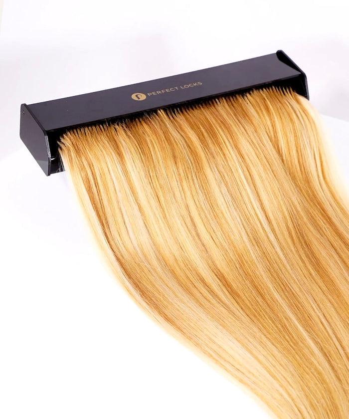 Sleek, long, blonde hair extensions cascade smoothly from a black Perfect Locks holder against a white background.