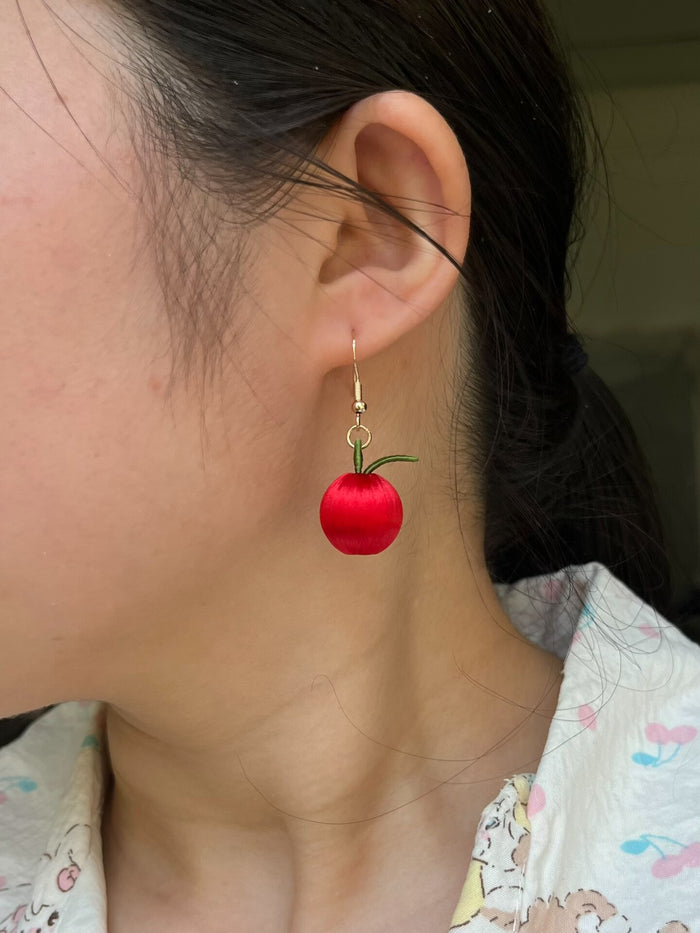 A pair of handmade Chanhua apple earrings worn on an ear
