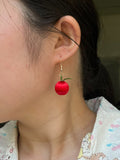 A pair of handmade Chanhua apple earrings worn on an ear