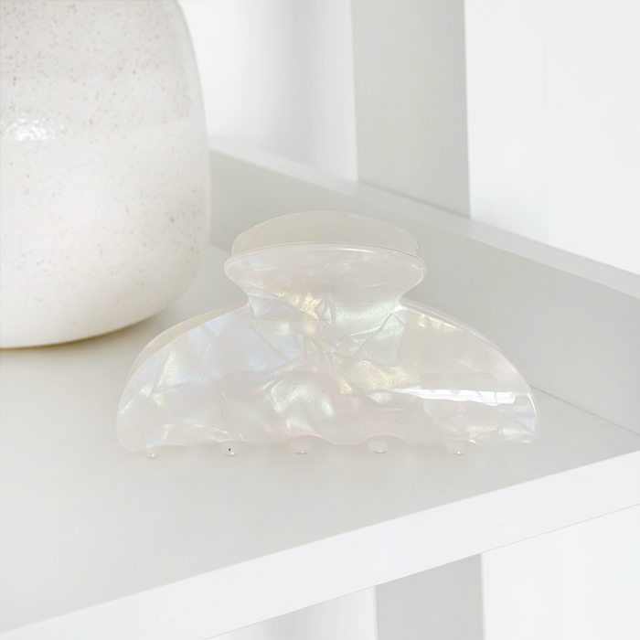 Iridescent pearl claw clip by Coconut Lane on a white shelf beside a textured white ceramic vase.