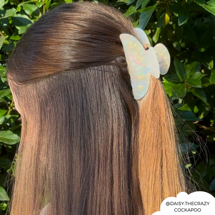Woman with long brown hair wears Coconut Lane iridescent pearl claw clip, standing outside with greenery behind her.