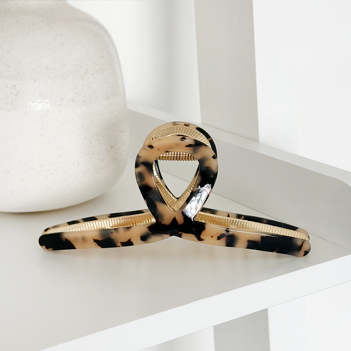 Ivory tortoiseshell claw clip by Coconut Lane on a white shelf next to a speckled white vase.