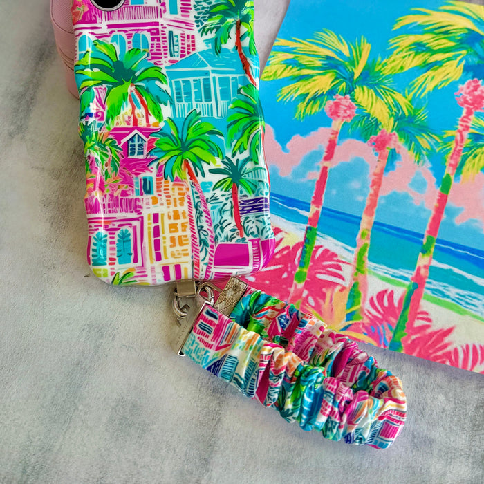 A vibrant La Palma Villa phone scrunchie wrist strap attached to a matching Wavy Luxe phone case with a colorful pink, green, and blue tropical palm tree print.