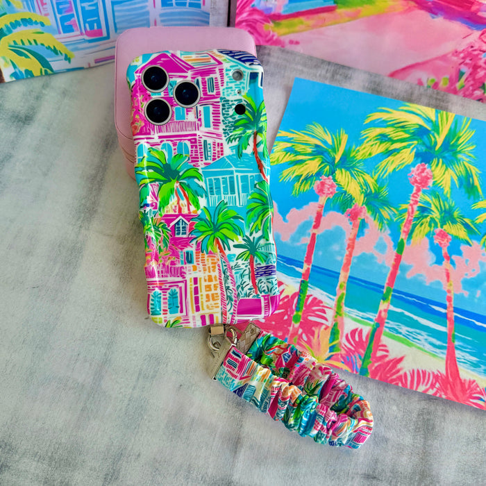 A vibrant La Palma Villa phone scrunchie wrist strap attached to a matching Wavy Luxe phone case with a colorful pink, green, and blue tropical palm tree print.