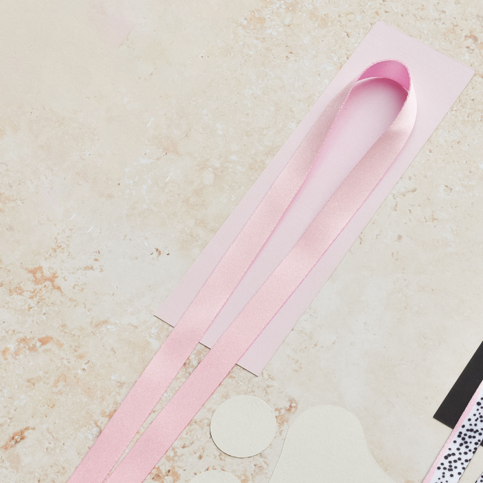 Plain baby pink Coconut Lane lanyard displayed on a light pink card with cutouts, set on a beige marbled background.
