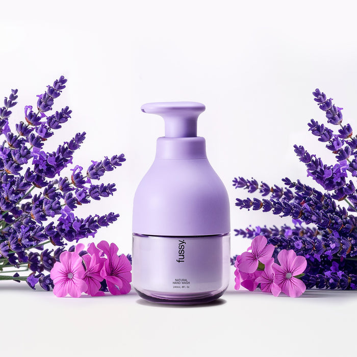Fussy's natural, refillable Lavender Fields hand wash in a Lilac pump bottle, set against a background of lavender and geranium flowers.