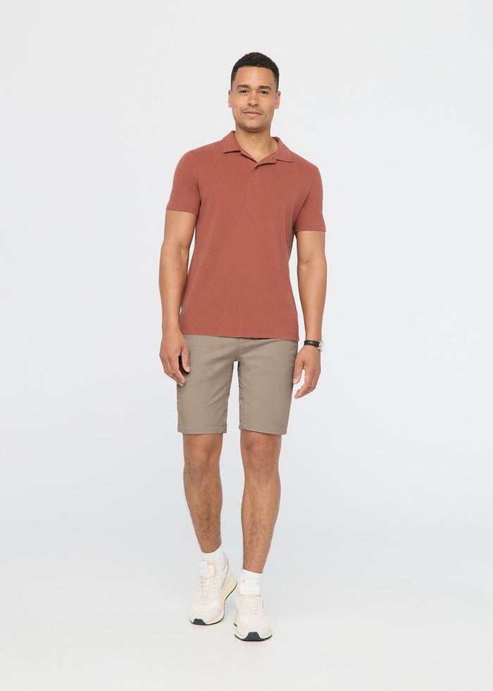 Man wearing a rust-colored polo shirt and sandstone knee-length shorts with white sneakers.