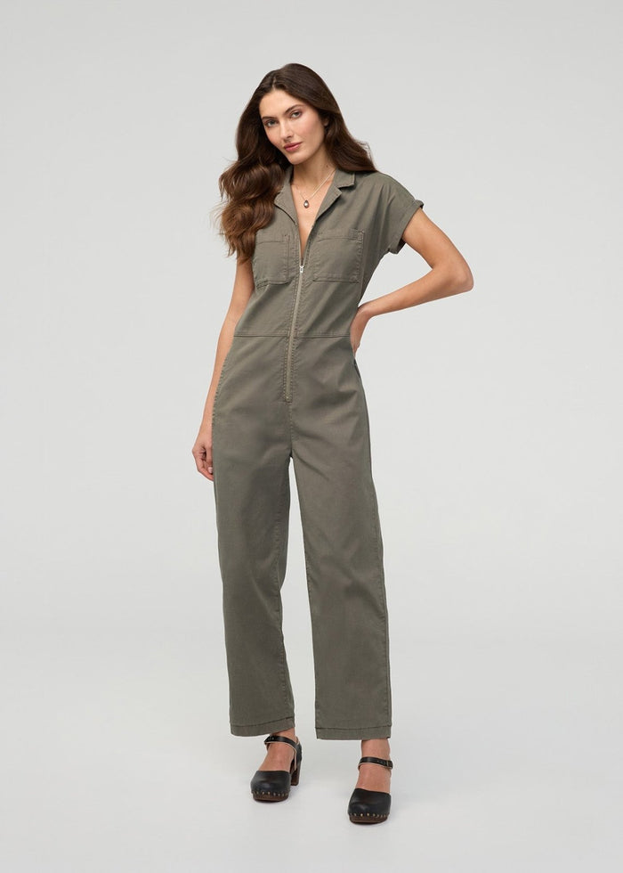 Thyme-colored boiler suit with short sleeves, front zip closure, and chest pockets worn with black platform sandals.