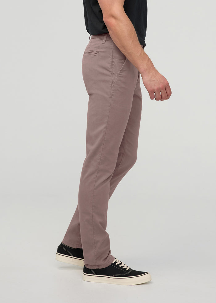 Man wearing mauve straight-leg chino pants with black shirt and black sneakers, shown from side view.