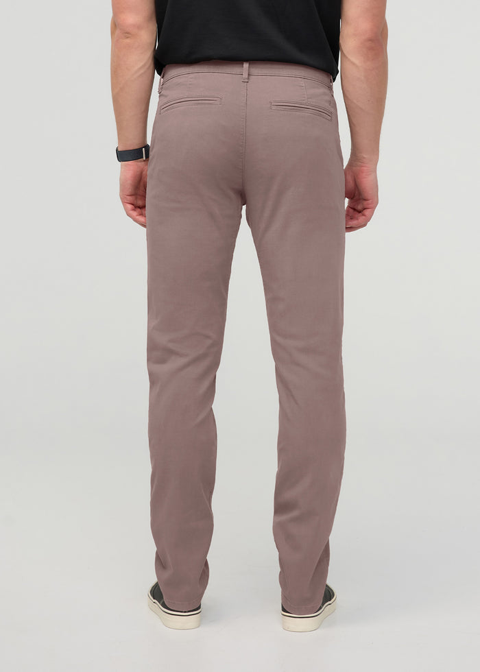 Rear view of mauve slim straight chino pants with back pockets on a model wearing a black shirt.