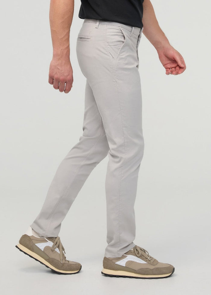 Man wearing light gray slim straight chino pants with black shirt and tan sneakers.