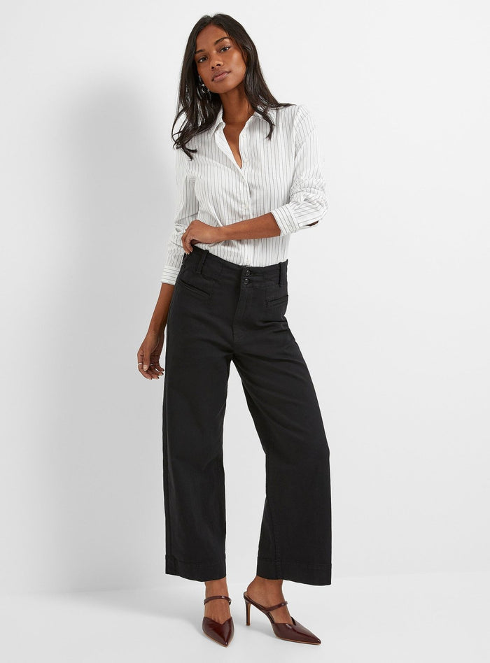 Black high-rise trousers with wide legs and button waistband, styled with white pinstriped shirt.