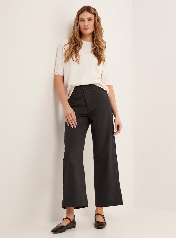 Woman wearing black high-rise straight-leg cropped trousers with a white t-shirt and black flats.