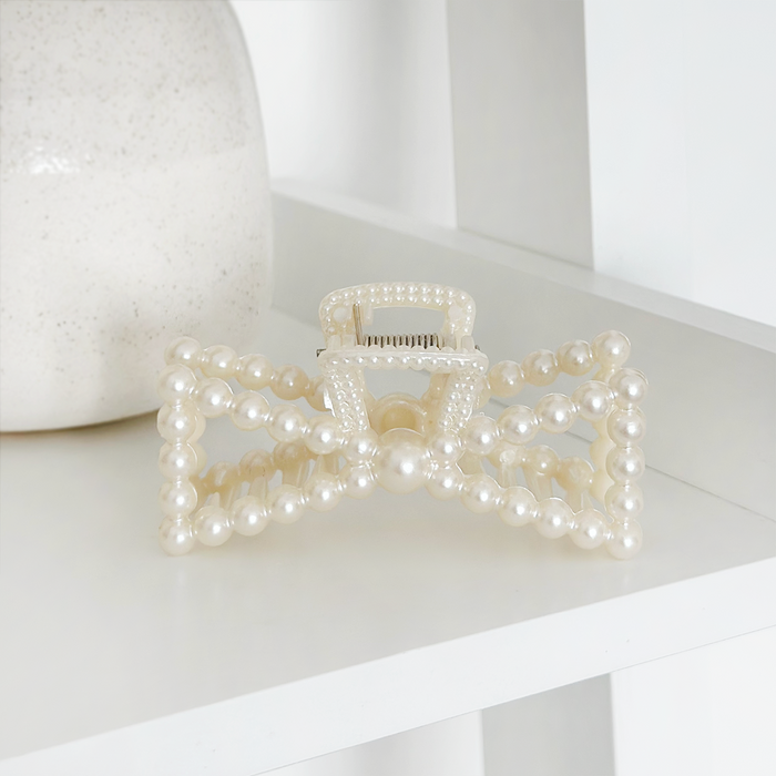 Pearl bow claw clip with a shiny finish sits next to a cream vase on a white shelf.