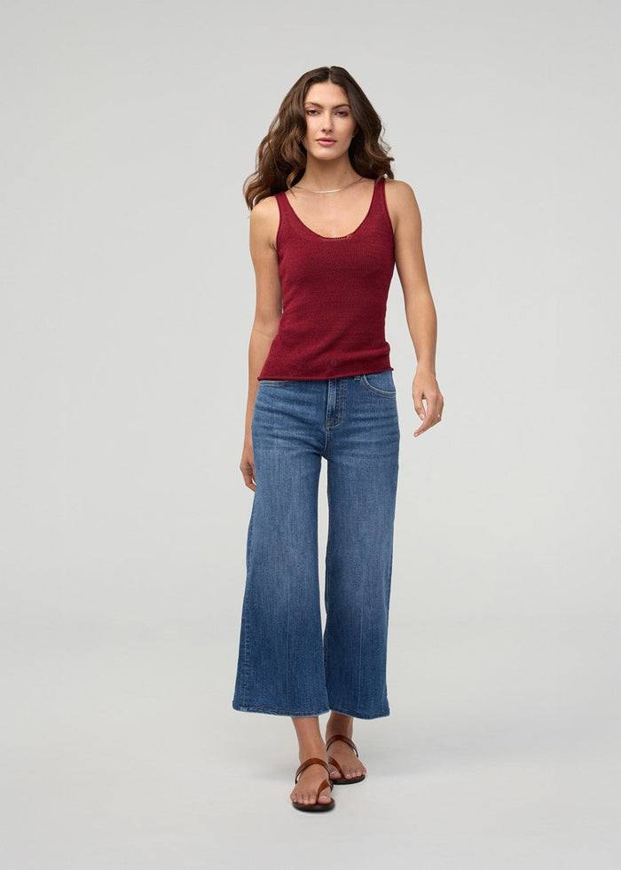 Woman wearing burgundy tank top with high-rise wide-leg cropped blue denim jeans and brown sandals.