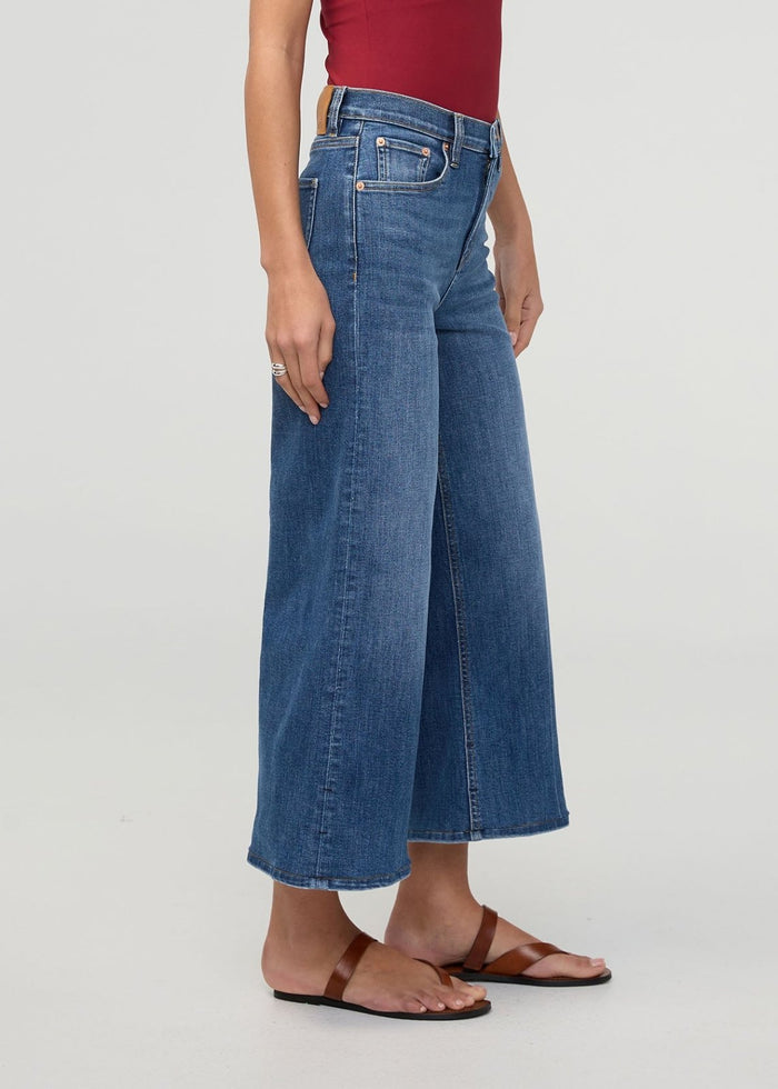 Woman wearing high-rise wide-leg cropped blue denim jeans with brown sandals and burgundy top.