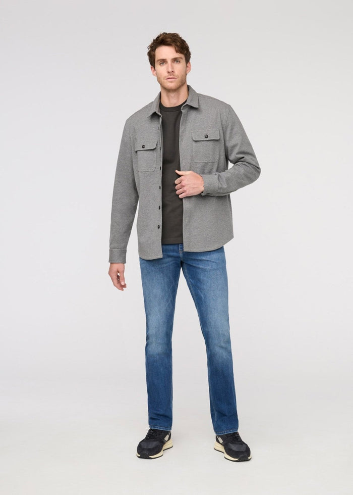 Man wearing a gray jacket, black shirt, blue jeans, and black shoes on a white background