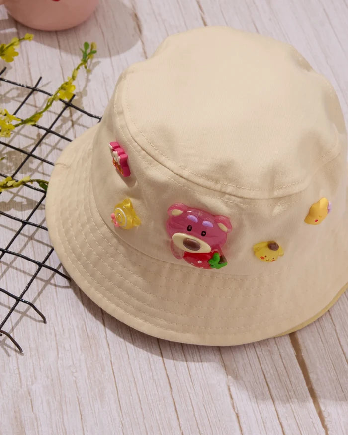 Kids beige bucket hat with colorful bear charm patch and small fruit-like appliques