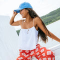 Woman wearing a blue cap and white top with red floral pants, standing outdoors.