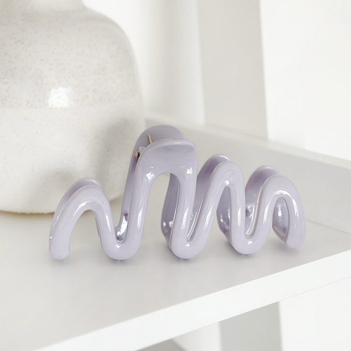 Lilac wavy squiggle claw clip by Coconut Lane on a white shelf next to a textured vase.