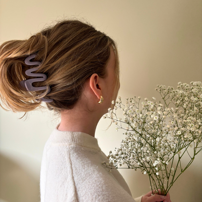 Woman wearing a lilac squiggle claw clip in her hair, white sweater, and gold earrings, holding babys breath flowers.