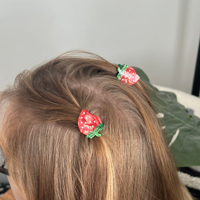 Blonde hair secured with small pink Coconut Lane strawberry-patterned claw clips.