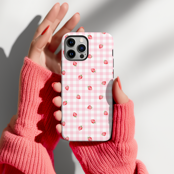 Hands in pink fingerless gloves hold a Coconut Lane gingham phone case with a ditsy strawberry pattern.