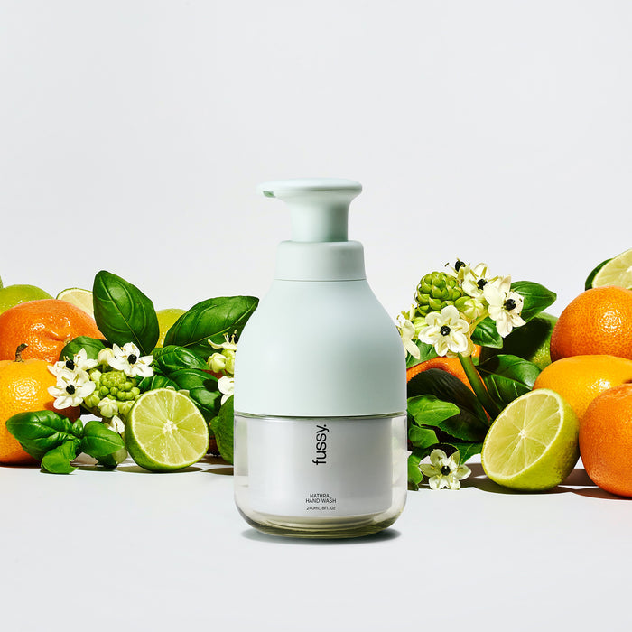 Fussy's natural, refillable Tropic Tonic body wash in a Mint Green pump bottle, set against a background of limes, marjoram and basil leaves