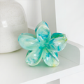 Blue and white marbled glass flower ornament next to a white vase and a Coconut Lane tropical flower-pattern claw clip.