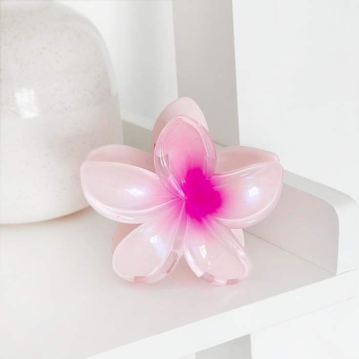 Pink Coconut Lane tropical flower claw clip with a bright center displayed on a white shelf next to a white vase.