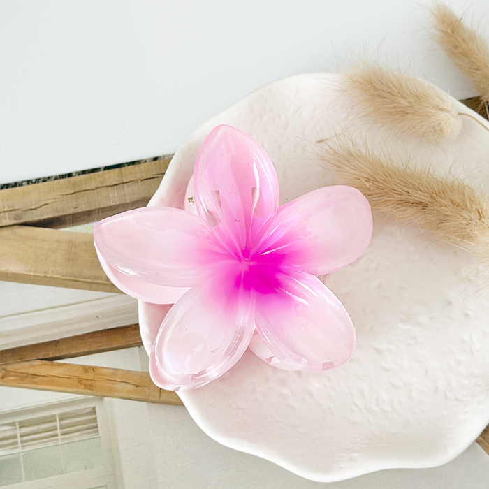 Pink tropical flower claw clip on a textured white plate next to dried grass accents.