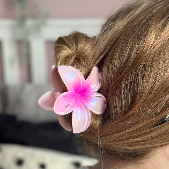Pink flower-shaped claw clip from Coconut Lane holds a brown-haired bun, with blurred background.