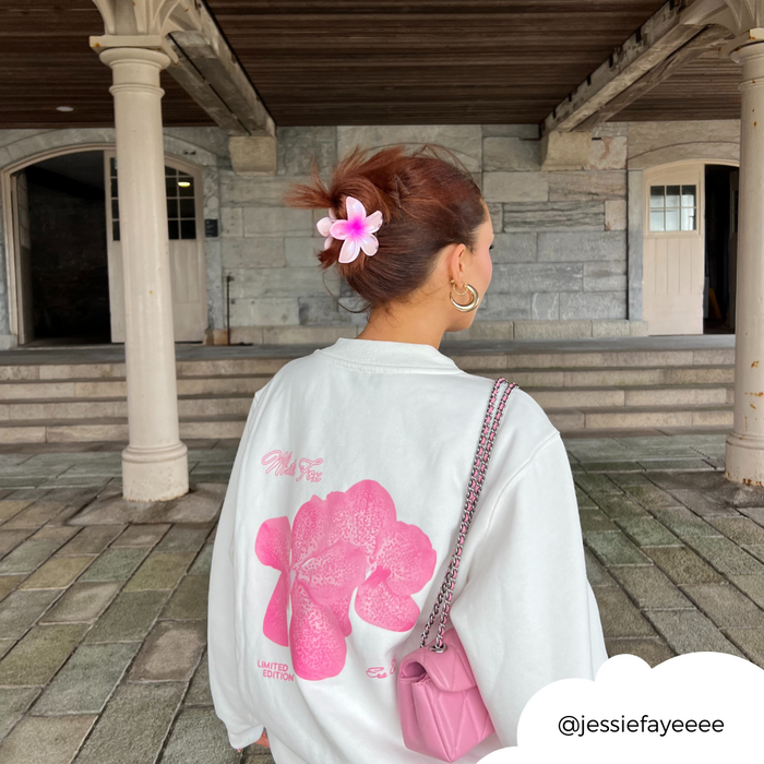 Woman wearing a pink Tropical Flower Claw Clip and holding a pink purse, dressed in a white sweatshirt with pink print.