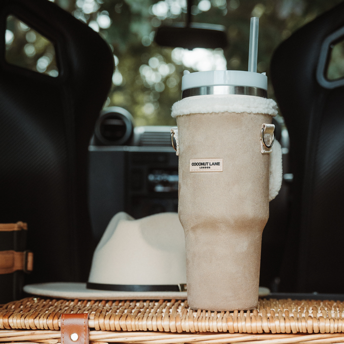 Nude Coconut Lane Tumbler Carry Case on a picnic basket inside a car, with a hat visible in the background.